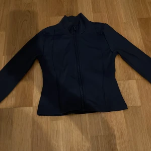 Svart jacka från Gina Tricot - Snygg svart jacka från Gina Tricot med dragkedja framtill. Jackan har en stilren design med långa ärmar och en hög krage. Perfekt för en cool och enkel look.