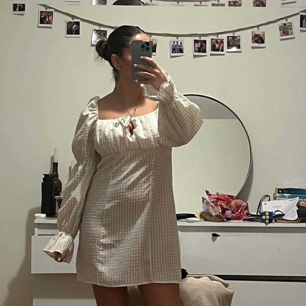 Charmig beige rutig klänning med långa puffärmar och en söt knytning framtill. Perfekt för en avslappnad och stilren look. Den har en kort längd och använt 2 gånger.. Mekot.