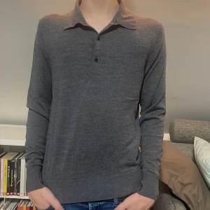 Grå merinoull pikétröja  - Snygg grå pikétröja med långa ärmar och knappar framtill. Perfekt för en stilren look. Tröjan har en klassisk krage och är tillverkad i ett merinoull material. Perfekt för er som är 160-170 och hör av er vid frågor och funderingar!