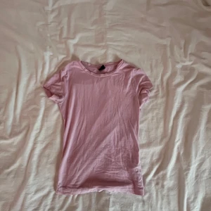 Rosa t-shirt från Gina Tricot - Säljer en söt rosa t-shirt från Gina Tricot i storlek XS. Den är kortärmad och gjord i mjukt bomullsmaterial, perfekt för en avslappnad stil. Passar bra till jeans eller kjol för en enkel look.