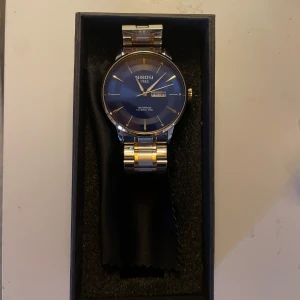 Blå klocka från Nibosi - Snygg klocka från Nibosi med blå urtavla och datumvisning. Armbandet är i silver och guld, vilket ger en elegant touch. Perfekt för den som vill ha en stilren accessoar. 