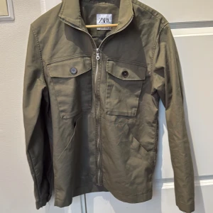 Olivgrön cardigan - Snygg olivgrön jacka från Zara med dragkedja och knappar på bröstfickorna. Jackan har en stilren design med långa ärmar och en klassisk krage. Cond 10/10