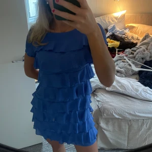 Blå klänning med volanger - Säljer en söt blå klänning med flera lager av volanger. Klänningen har korta ärmar och en rund halsringning. Perfekt för en somrig look! 💙 storlek 38 men passar mig som vanligtvis bär 34-36