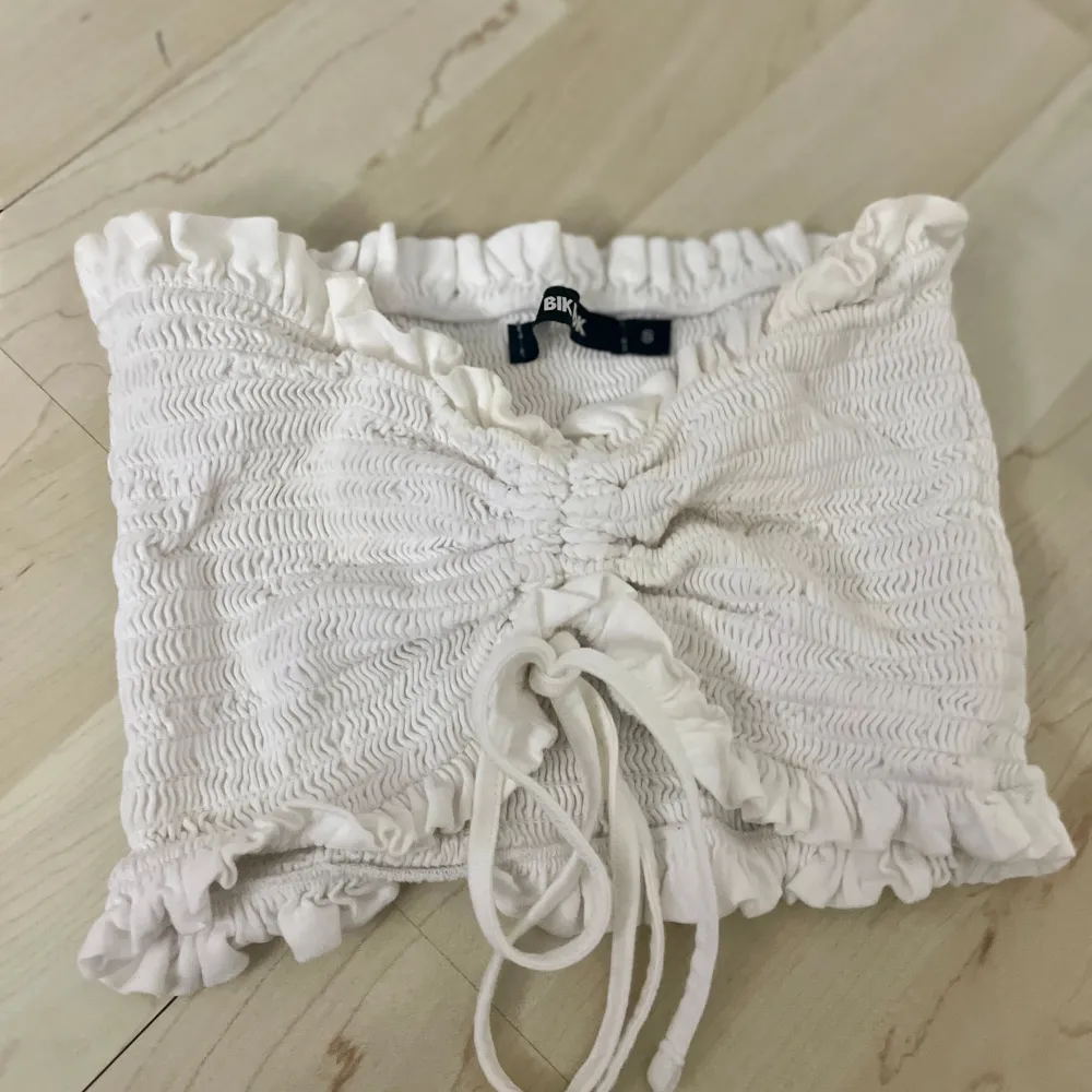 En vit topp med strechigt ribbat material. Endast använd få gånger tidigare. Har snören för att anpassa storleken till önskad passform. Passar perfekt med en kjol och en blazer över🌺. Yläosat.