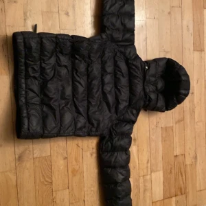 Svart pufferjacka med huva - Säljer en svart pufferjacka med huva. Jackan har en dragkedja framtill och är quiltad för extra värme. Perfekt för kyliga dagar.
