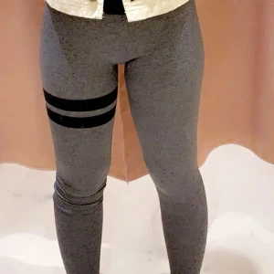 Grå leggings med svarta ränder - Snygga grå leggings med två svarta ränder runt ena låret. Perfekta för en sportig look eller avslappnad stil. De är stretchiga och bekväma, vilket gör dem idealiska för både träning och vardag.