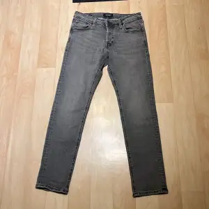 Säljer ett par grå slim fit jeans från Jack & Jones i storlek 30/30. De är i bra skick och har en klassisk femficksdesign med dragkedja och knapp. Perfekta för både vardag och fest!