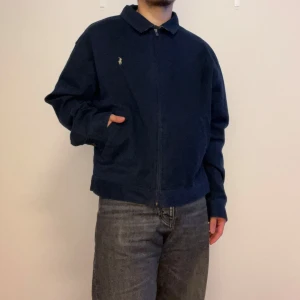 Mörkblå jacka från Polo Ralph Lauren - Säljer en snygg mörkblå jacka från Polo Ralph Lauren i storlek XL. Jackan är i bomull och har en dragkedja framtill. Den har en klassisk krage och långa ärmar med knappar vid ärmsluten. 