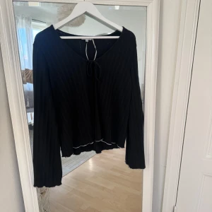 Svart ribbad tröja med knyt - Säljer en svart ribbad tröja med långa ärmar och en söt knytning framtill. Den har en lätt croppad stil med vågig kant nertill. Perfekt för höst och vår, och funkar både till vardags och fest. Superfin och i bra skick! Köpt för 549kr och inte använd