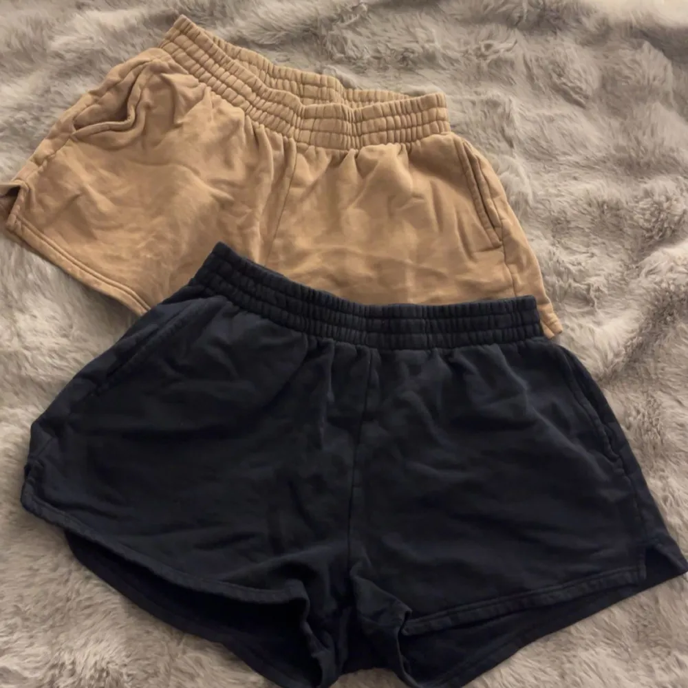 Säljer två par shorts från Gina Tricot i storlek M. Ett par är beige och det andra är svart. De har en elastisk midja för en bekväm passform. Perfekta för avslappnade dagar eller träning. Materialet känns mjukt och skönt mot huden.. Shorts.