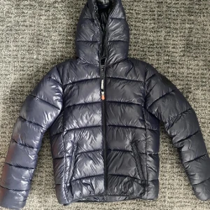 Svart pufferjacka från Save the Duck - Säljer en mörk blå pufferjacka från Save the Duck i mycket bra skick. Jackan är ultralätt och har en dragkedja framtill. Perfekt för kalla dagar med sin quiltade design och huva. Skriv i dm vid några funderingar.