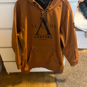 Skidjacka från Slade Couture - Säljer en snygg brun skidjacka ”hoodie” från Slade Couture i storlek 44. Den har en stor ficka fram och coola svarta detaljer med text. Använd under 1vecka i fjällen. 