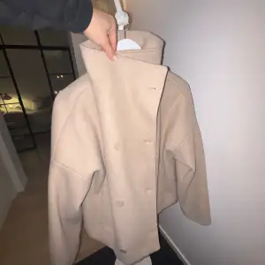 Säljer en superfin beige kappa från NA-KD i mycket bra skick. Den har en stilren design med knappar framtill och hög krage. Perfekt för höst och vår, och den är gjord i ett mjukt material som känns lyxigt. Passar både till vardags och fest! Nypris 600kr