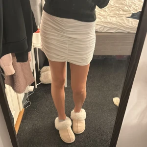 Vit tight kjol - Säljer en superfin vit kjol i mycket bra skick. Den har en snygg rynkad detalj på sidorna som ger en extra touch. Perfekt för sommarens alla fester eller en utekväll med vännerna. Passar bra med både sneakers och klackar!