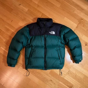 The North Face Jacka Grön - The North Face 1996 Retro Nuptse 700 dunjacka  i storlek M. Jackan är i mycket bra skick och perfekt för kalla vinterdagar. Den har en ykk dragkedja framtill och är långärmad med justerbara snören i nederkant. Utrustad med 2 ytterfickor och en inre. Använd 5 gånger. Köpt på Caliroots för 3500kr. Kvitto ska finnas. 