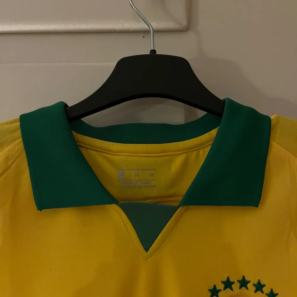 Säljer en gul Brasilien fotbollströja från Nike med gröna detaljer och nummer 10 på både fram- och baksidan. Tröjan har korta ärmar och en klassisk krage. Perfekt för fotbollsfans som älskar Brasilien! 🟡🟢Storlek XS. T-shirts.