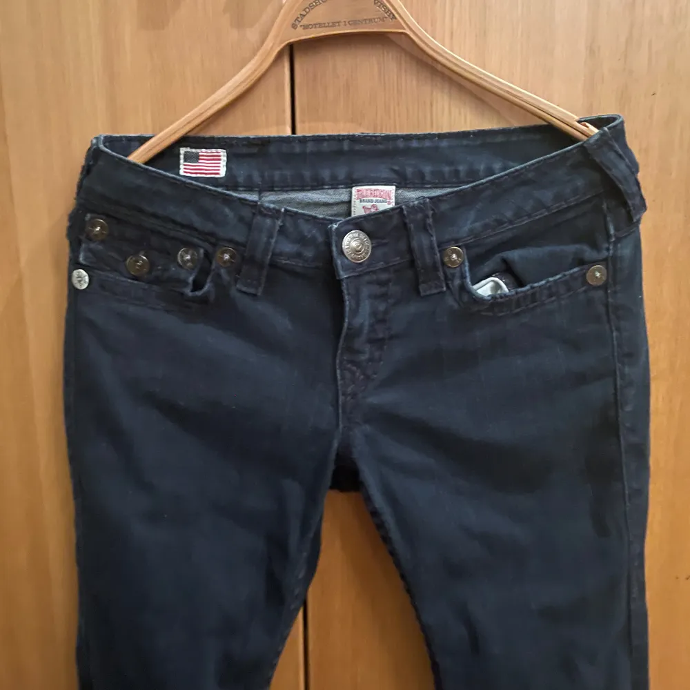 Säljer ett par snygga mörkblå jeans från True Religion. De har en tight passform och är i mycket bra skick. Jeansen har coola detaljer som knappar och fickor med lock baktill. Perfekta för både vardag och fest!. Jeans & Byxor.