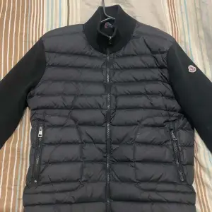 Säljer en snygg svart quiltad jacka från Moncler. Den har långa ärmar och dragkedja framtill. Perfekt för höst och vår, med en stilren design och Moncler-logga på ärmen. Jackan är i mycket bra skick och passar både till vardags och lite finare tillfällen.