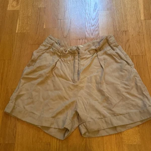 Beige shorts från Indiska - Säljer ett par snygga beige shorts från Indiska i storlek M. De är gjorda av 100% tencel vilket gör dem supermjuka och sköna. Perfekta för sommardagar! Shortsen har en normal passform med dragkedja och knapp framtill. De har också två fickor bak. 🩳✨