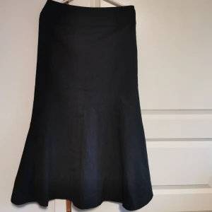 Svart kjol från b.young - Snygg svart kjol från b.young i storlek EU 36. Kjolen har en elegant och klassisk design med en diskret dragkedja baktill. Perfekt för både vardag och festliga tillfällen. Materialet känns bekvämt och har en lätt struktur som ger en fin passform.