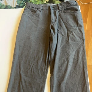 Grå byxor från Carhartt - Säljer ett par grå byxor från Carhartt i relaxed fit. De är i bra skick och har en klassisk design med fem fickor och bälteshällor. Perfekta för vardagsbruk eller arbete. Byxorna är tillverkade i slitstarkt material och har en knappgylf.