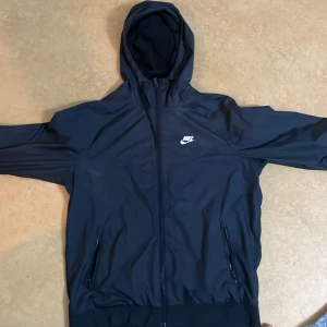 svart hoodie från Nike - Säljer en snygg svart hoodie från Nike i storlek M. Den har en dragkedja framtill och två fickor med dragkedjor. Perfekt för höst och vår, med en skön passform och Nike-logga på bröstet. Huvan ger extra skydd mot väder och vind. Perfekt för både träning och vardag!