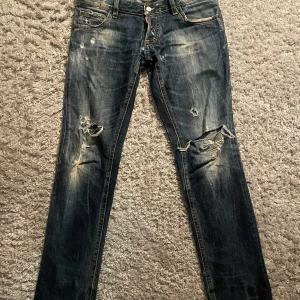 Blå jeans från Dsquared - Säljer ett par snygga blå jeans från Dsquared i bra skick. De har en snygg slitning och lite färgstänk för en unik look. Perfekta för en avslappnad stil med en touch av edge. Passar bra till både vardag och fest! används inte längre där av de låga priset. pris kan diskuteras kom med förslag.