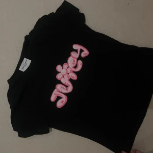 Juicy couture  - Säljer en svart t-shirt från Juicy Couture med ett stort rosa och vitt Juicy-tryck på framsidan. T-shirten är kortärmad och i bomull, perfekt för en avslappnad stil. Den är i bra skick och redo för nya äventyr!