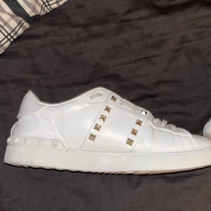 Valentino rockstud - Säljer ett par snygga vita sneakers från Valentino i bra skick. De har coola nitar på sidorna och över snörningen som ger en edgy look. Perfekta för både vardag och fest! Skorna är i skinn och har en klassisk design med en modern twist.