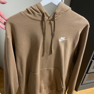 Beige hoodie från Nike - Säljer en snygg beige hoodie från Nike i storlek M. HELT NY SKICK! Aldrig använt. Den har en klassisk design med en känguruficka och justerbar huva. Perfekt för både vardag och en chill hemma kväll. Nike-loggan är broderad i vitt på bröstet. Dm om frågor och pris kan diskuteras!