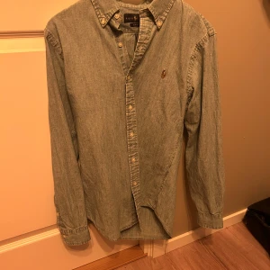 Jeans skjorta från Ralph Lauren - Säljer en snygg jeans skjorta från Ralph Lauren i slim fit. Skjortan är i bomull och har långa ärmar med knappar framtill. Perfekt för både vardag och fest! 🕺