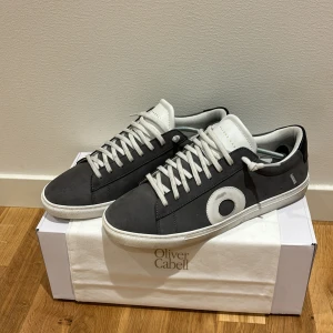 Grå och vita sneakers från Oliver Cabell - Säljer ett par Oliver Cabell sneakers i grått och vitt. Skorna är i storlek 42 och dom är perfekta för både vardag och fest! De är i mycket bra skick och kommer i originalförpackning och en skopåse  från Oliver Cabell. 