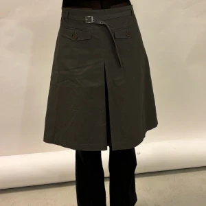 Grå kjol med bälte - Snygg grå kjol i normal passform med ett coolt bälte i midjan. Kjolen har en stilren design med en slits framtill och dekorativa knappar. Perfekt för både vardag och fest! 🖤