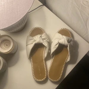 Vita sandaler med knyt - Säljer ett par vita sandaler i mycket bra skick. De har en snygg knytning på ovansidan och en bekväm sula. Perfekta för sommardagar och stranden. De är i storlek 39 men passar 38, Aldrig använda!
