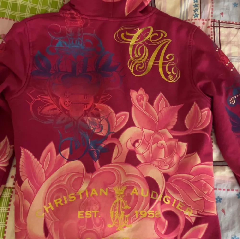 Säljer en supercool jacka från Christian Audigier i en härlig rosa färg med färgglada blommönster och text. Jackan har dragkedja och huva med snygga snören. Insidan är mönstrad med kedjor och kronor. Perfekt för att sticka ut i mängden! Köpts HELT NY OANVÄND, högt värde och priset kan diskuteras . Jackor.