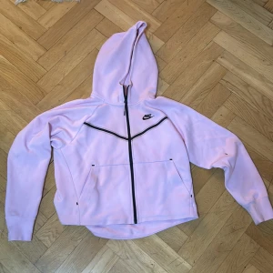 Ljusrosa hoodie från Nike - Säljer en superfin ljusrosa hoodie från Nike i storlek S. Den har en dragkedja framtill och en mysig huva. Perfekt för kyliga dagar eller som ett snyggt lager på väg till gymmet. Den är i bra skick och redo för nya äventyr! 💖