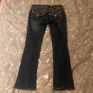 Mörkblå jeans från Miss Me - Säljer ett par snygga mörkblå jeans från Miss Me i storlek 26. De är bootcut och har glittriga detaljer och broderier på bakfickorna. Superbra gick, säljer då dom tyvärr inte kommer till användning längre 💗