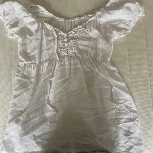 Vit blus  -  vit blus med spetsdetaljer framtill. Den har korta ärmar och en luftig passform, perfekt för varma sommardagar. Blusen är i ett lätt och bekvämt material som ger en romantisk känsla.