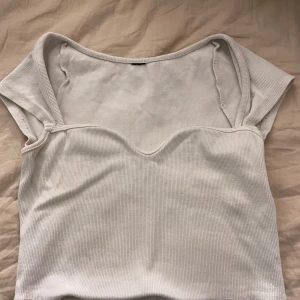 Vit ribbad croppad topp - Säljer en superfin vit ribbad topp som är croppad och har en unik offshoulder-design. Perfekt för sommardagar eller en utekväll. Tröjan sitter även ganska tight 