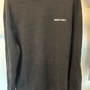 Svart tröja från Axel Arigato - Säljer en stilren svart tröja från Axel Arigato med trycket 'ARIGATO ©2014' på både fram- och baksidan. Tröjan har en cool papegojdetalj på ryggen. Den är långärmad och gjord av mjuk bomull, perfekt för en avslappnad look.