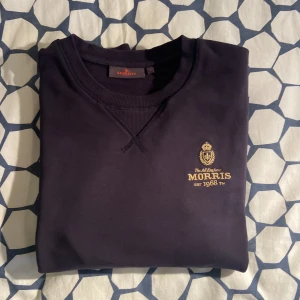 Mörkblå tröja från Morris - Säljer en snygg mörkblå tröja från Morris med ett stilrent tryck på bröstet. Tröjan är i storlek S och har långa ärmar. Perfekt för både vardag och lite finare tillfällen. Den är i bra skick och redo för en ny ägare! Skicka gärna pris förslag!
