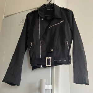 Svart jacka från Boohoo - Säljer en snygg svart jacka från Boohoo i storlek 40. Den har en cool bikerstil med dragkedjor och ett bälte i midjan som går att ta bort. Jackan är långärmad. Den är i bra skick. Alla kläder är tvättade som inte är nya med lappar. 