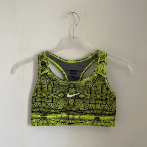 Gul och svart sporttopp från Nike - Säljer en cool sporttopp från Nike i storlek S. Den är lime grön med ett svart, abstrakt mönster och har en klassisk racerback-design. Perfekt för träning och ger bra stöd. Materialet är stretchigt och bekvämt.