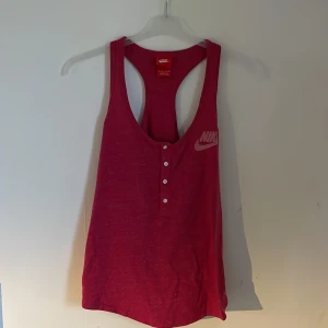 Rosa linnetopp från Nike - Säljer en snygg rosa linnetopp från Nike. Den är ärmlös och har en djup urringning med knappar framtill. Perfekt för träning eller en varm sommardag. Toppen är i bra skick och superbekväm att ha på sig!