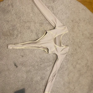 Beige ribbad bodysuit - Säljer en stilren beige bodysuit med ribbad struktur. Den har långa ärmar och en rund halsringning. Perfekt för lager-på-lager eller att bära som den är. Passar till många olika stilar och tillfällen.