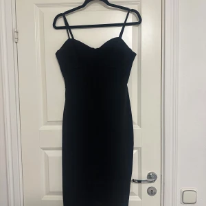 Svart klänning med smala axelband - Elegant svart klänning med smala axelband och figurnära passform. Perfekt för en stilren look. Klänningen har en enkel och tidlös design som passar många tillfällen.