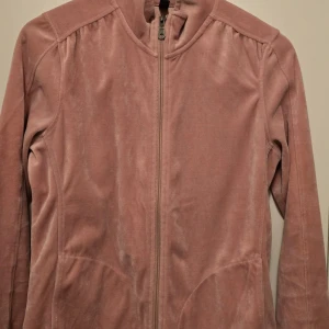 Rosa velourjacka från Soyaconcept - Mysig rosa velourjacka från Soyaconcept med dragkedja framtill. Perfekt för en avslappnad stil. Jackan har långa ärmar och en mjuk känsla med byxorna. 