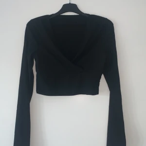 Svart omlottopp från Shein - Säljer en svart omlottopp från Shein i storlek XS. Toppen är croppad med långa ärmar och har en stilren design. Perfekt för att skapa en trendig look.