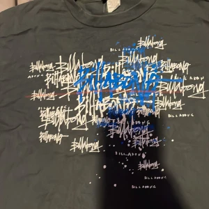 Grå t-shirt från Billabong - Säljer en grå t-shirt från Billabong med ett coolt grafiskt tryck i blått och vitt. T-shirten är tillverkad i 100% bomull och har en normal passform. Perfekt för en avslappnad stil.