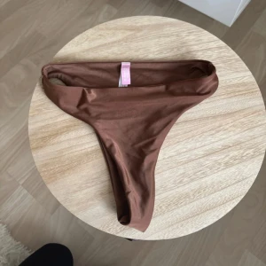Brun bikiniunderdel - Snygg brun bikiniunderdel i en enkel och stilren design. Perfekt för en dag på stranden eller vid poolen. Den har en klassisk passform och är tillverkad i ett mjukt och bekvämt material. Varan är aldrig använd
